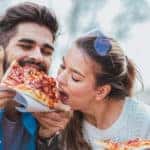 Couple eating pizza outdoors and smiling.They are sharing pizza in a outdoor cafe.