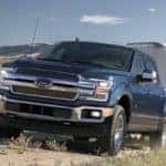 2019 Ford F-150 towing trailer on dirt path with horses in background