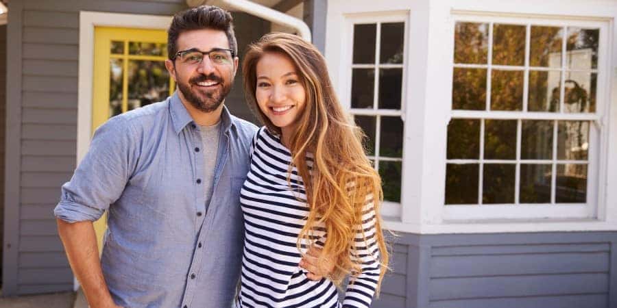 A man and woman smiling next to a house | Graff Chevrolet in Grand Prairie, Texas