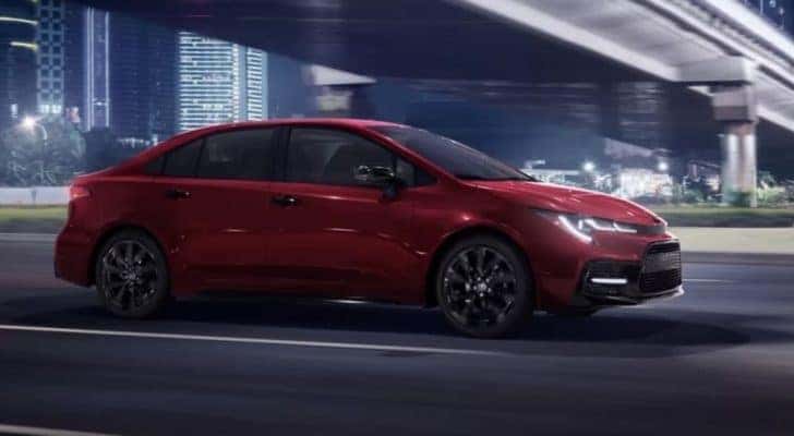 A red 2022 Toyota Corolla SE is shown driving past a city bridge at night.