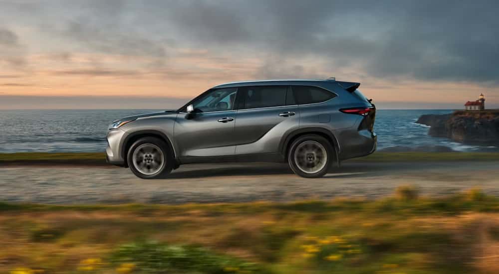 Side profile of a grey 2026 Toyota Highlander driving down the road. 