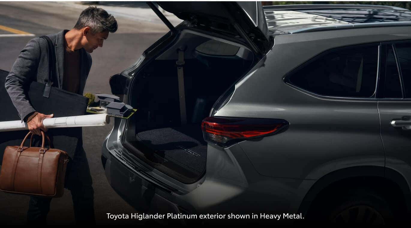 Rear crop view of a Toyota Highlander Platinum with open trunk as a man loads architectural plans.