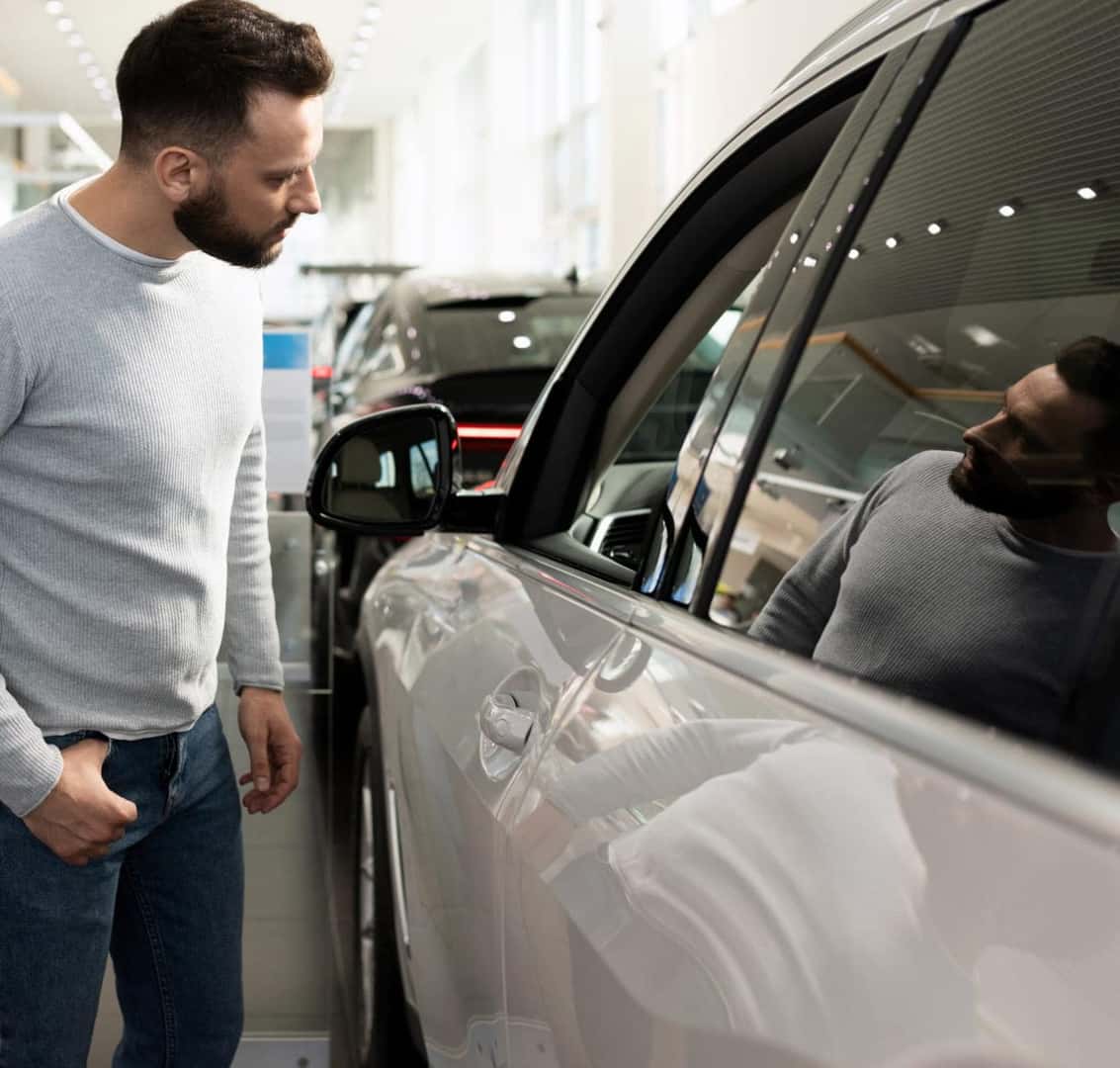 Man examining the exterior of a vehicle inside a dealership showroom.