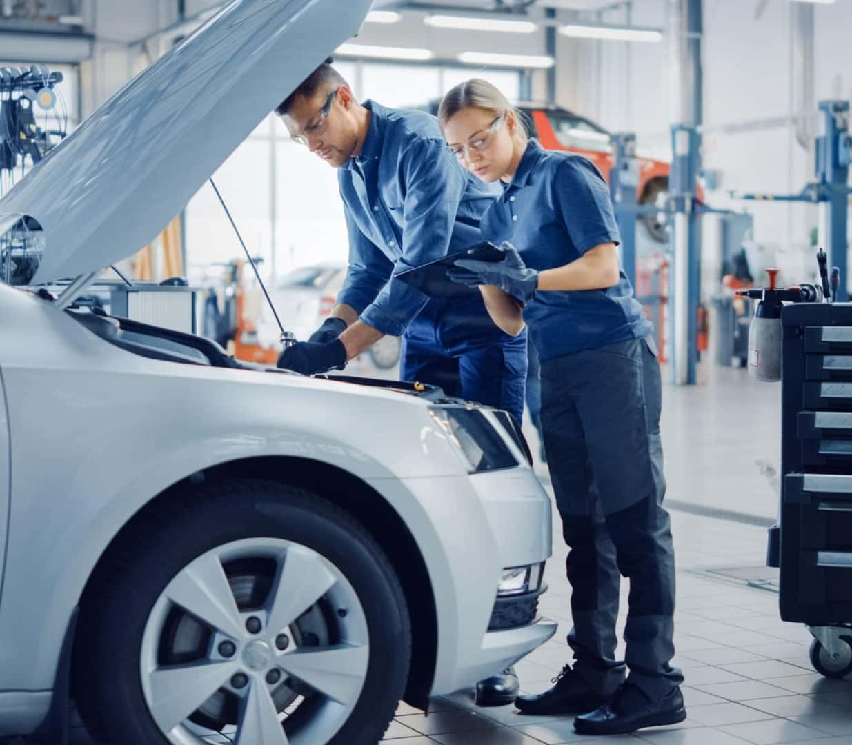 Two automotive technicians inspecting a vehicle with its hood open inside a service center.