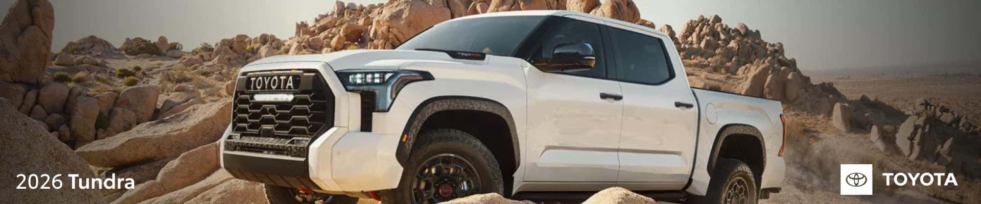 White 2026 Toyota Tundra driving through a rugged rocky desert landscape.