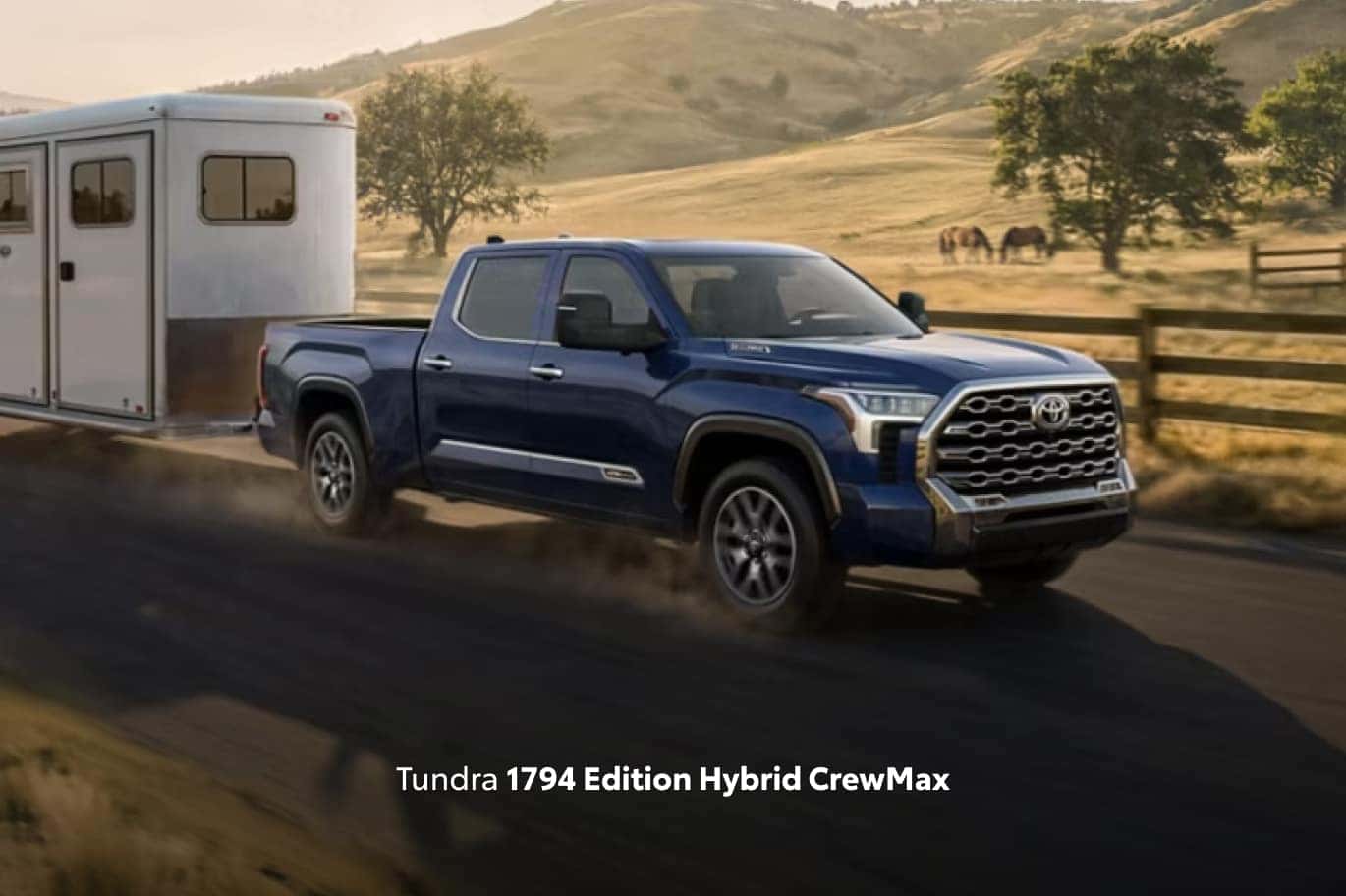 Blue Toyota Tundra 1794 Edition Hybrid CrewMax towing a horse trailer through a rural landscape.