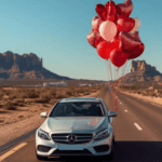 Silver Mercedes-Benz sedan driving on desert highway with red heart balloons tied to roof.