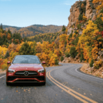 Red Mercedes-Benz driving along a winding mountain road surrounded by colorful fall foliage