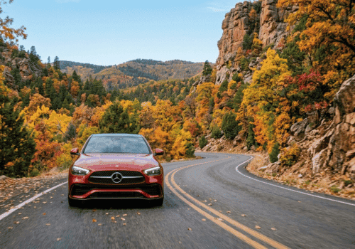 Red Mercedes-Benz driving along a winding mountain road surrounded by colorful fall foliage