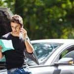 Man leaning against hood of broke down car on the side of the road talking on the phone