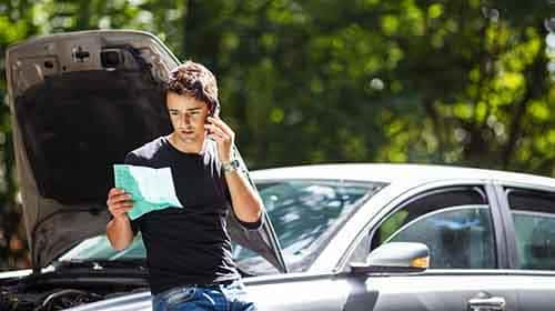 Man leaning against hood of broke down car on the side of the road talking on the phone