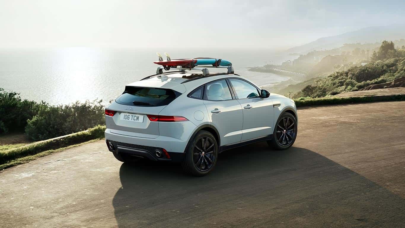 2018 Jaguar E-PACE driving near beach with surf board attached on top rails