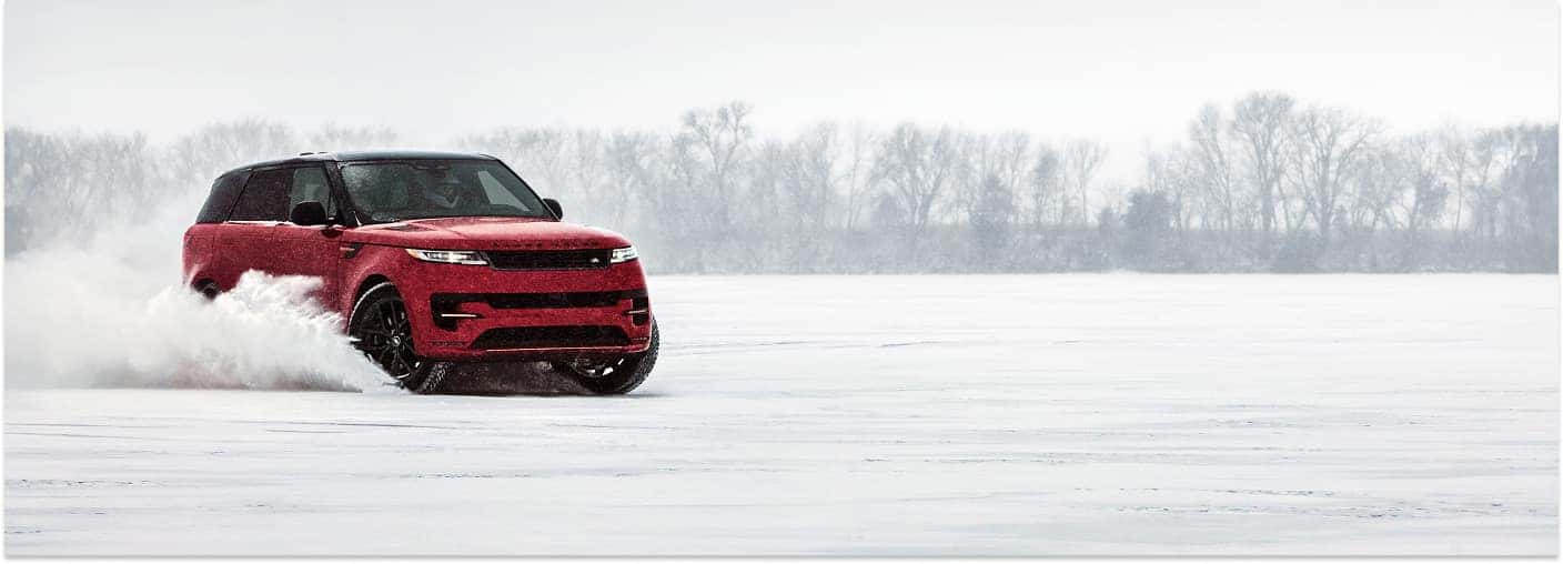 Front three-quarter view of a red 2025 Range Rover Sport driving on a frozen, snow-covered surface.