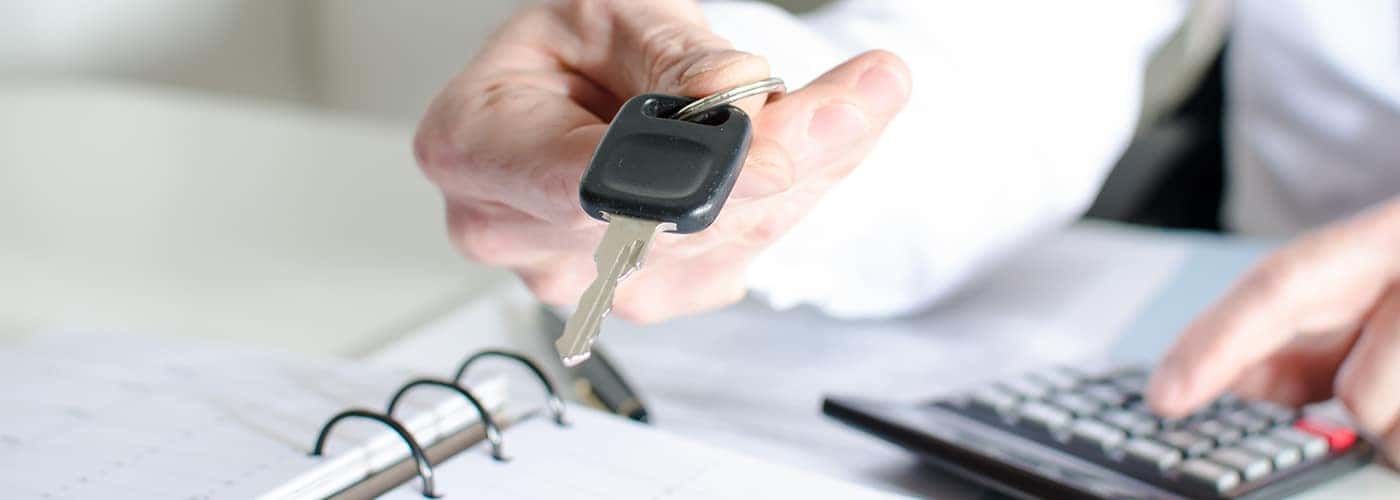 Car salesman holding a key and calculating a price at the dealership office