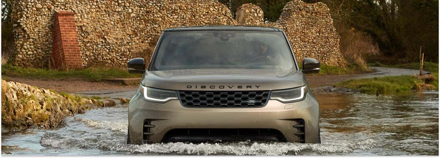 Front view of a bronze 2026 Land Rover Discovery SUV driving through shallow water.