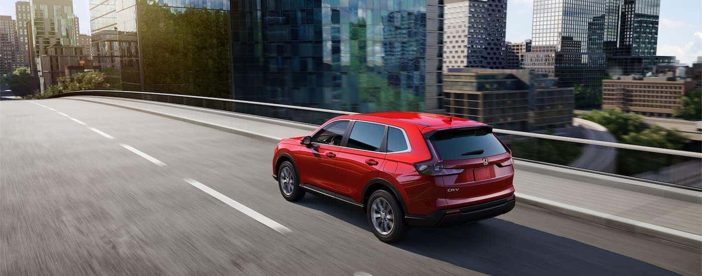 Rear view of a red 2025 Honda CR-V EX driving into a city.