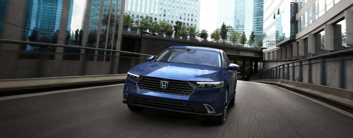 A blue 2025 Honda Accord Touring Hybrid driving up a highway ramp through a city.