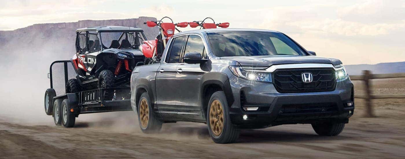 A silver 2022 Honda Ridgeline RTL-E towing a trailer with ATVs.