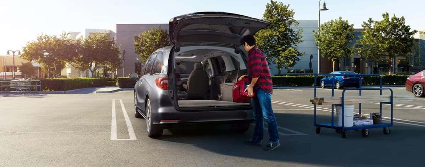 A person is shown loading gear into a grey 2023 Honda Odyssey.