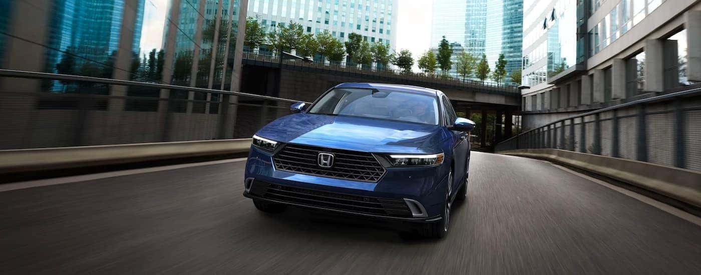 A blue 2023 Honda Accord Touring Hybrid driving across a bridge from a dealer with a Honda Accord for sale.