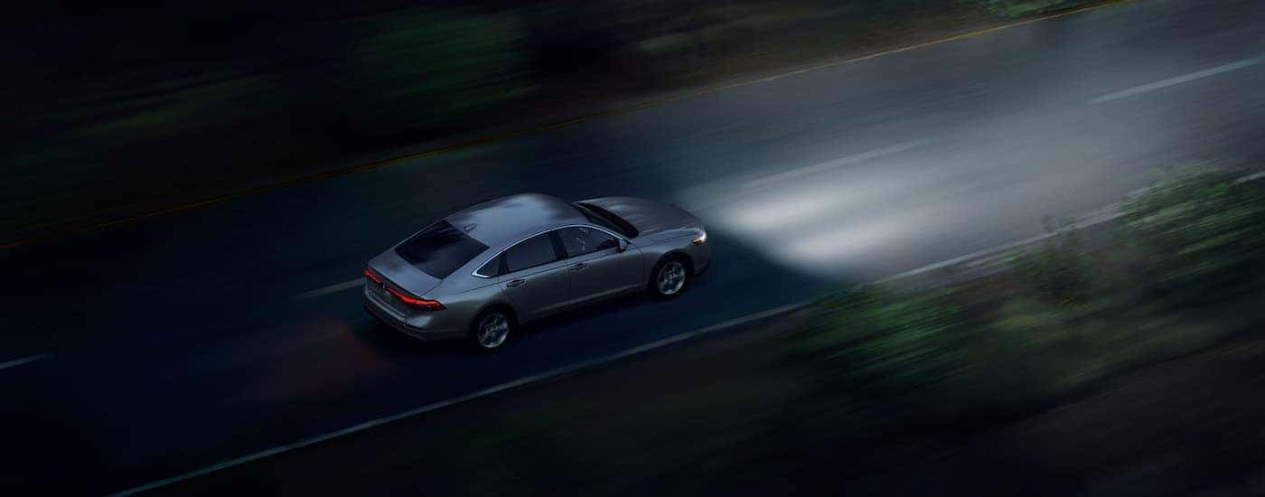 A grey 2025 Honda Accord Hybrid driving on a road at night.