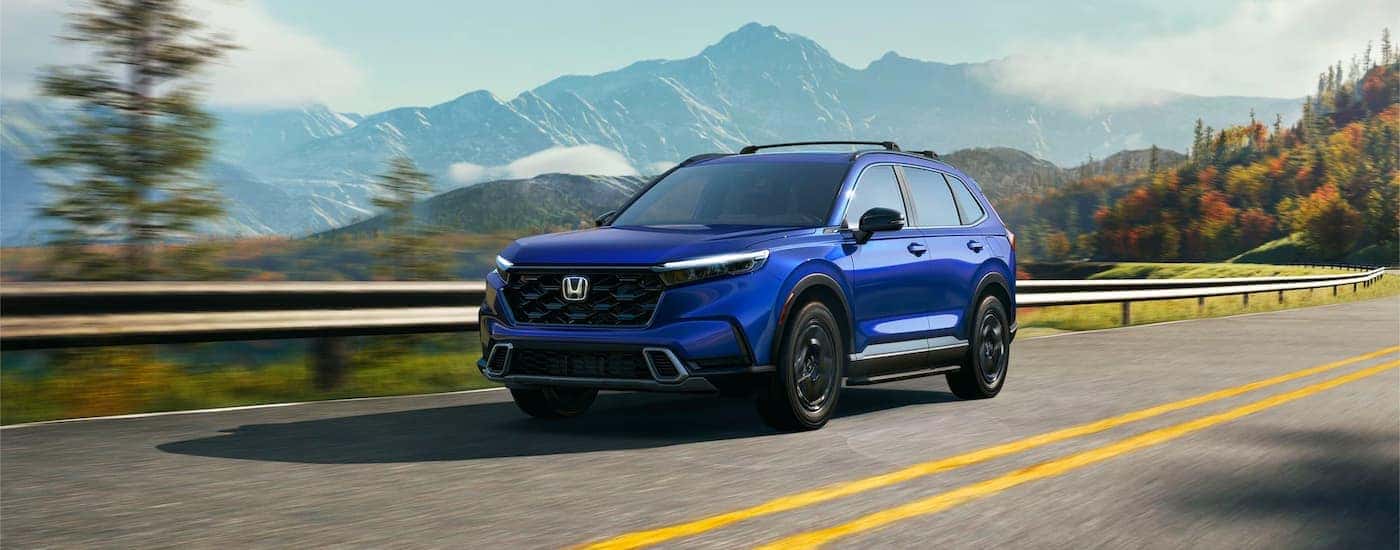 A blue 2024 Honda CR-V Hybrid Sport Touring for sale near East Hartford driving down an open road.