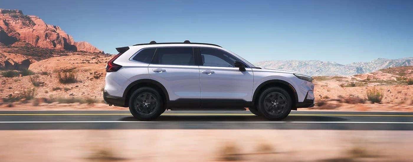 Side view of a white 2023 Honda CR-V Sport Touring Hybrid driving on an open road.