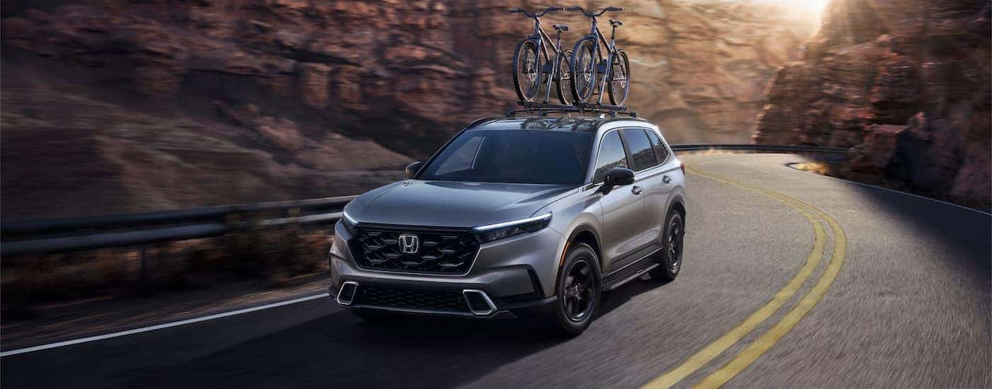 A grey 2025 Honda CR-V Sport Touring Hybrid for sale near Middletown driving down a winding road.