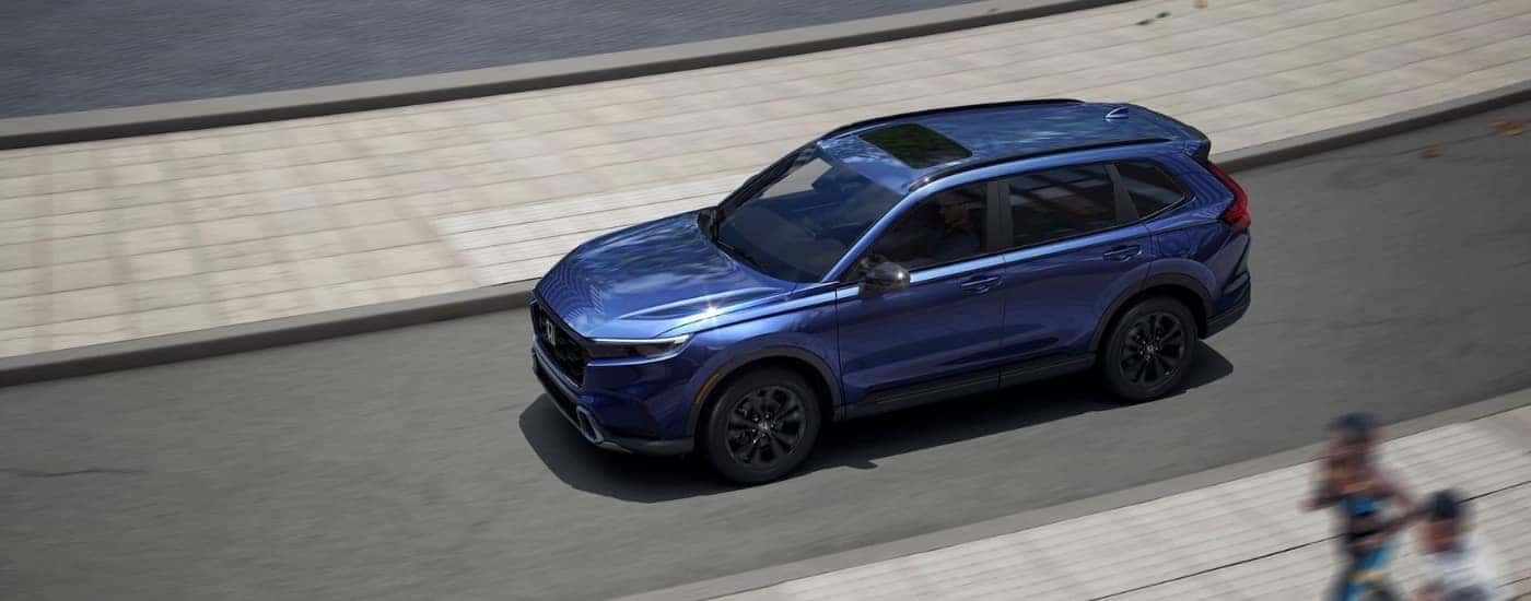 Overhead view of a blue 2025 Honda CR-V Hybrid Sport Touring driving on a city street.