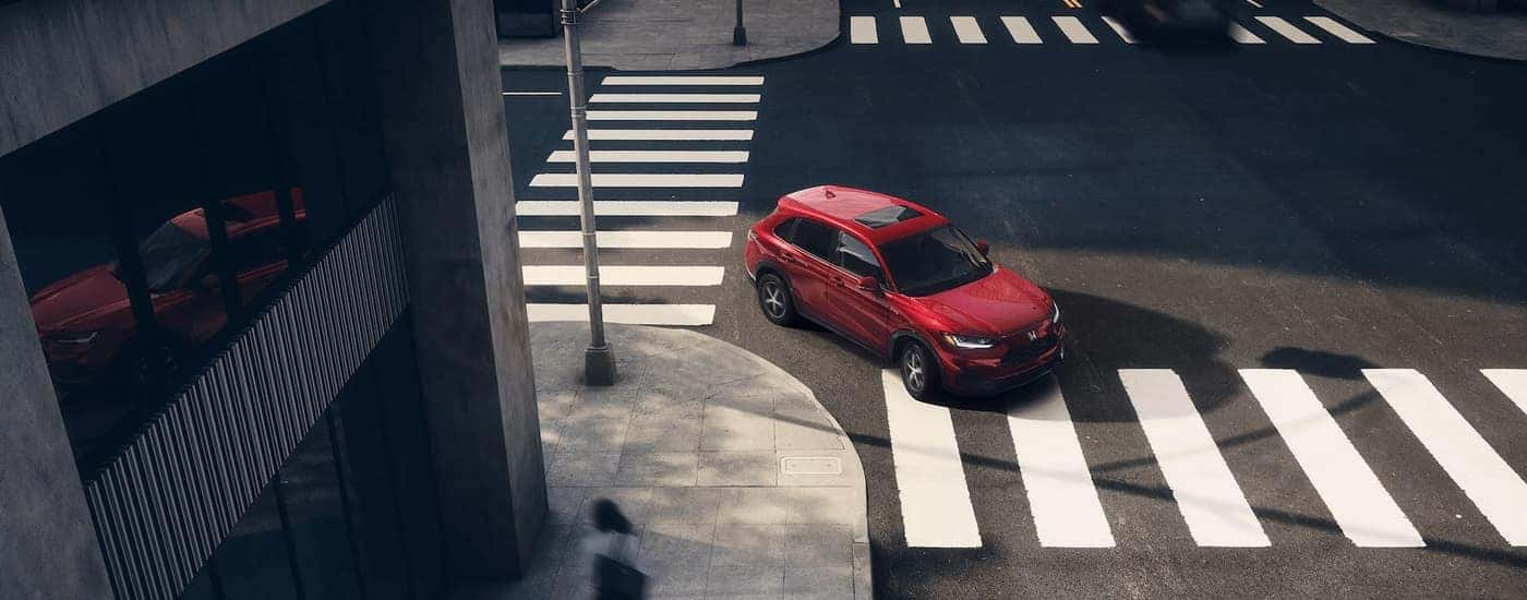 A red 2025 Honda HR-V EX-L is driving through a city intersection to a Honda dealer.
