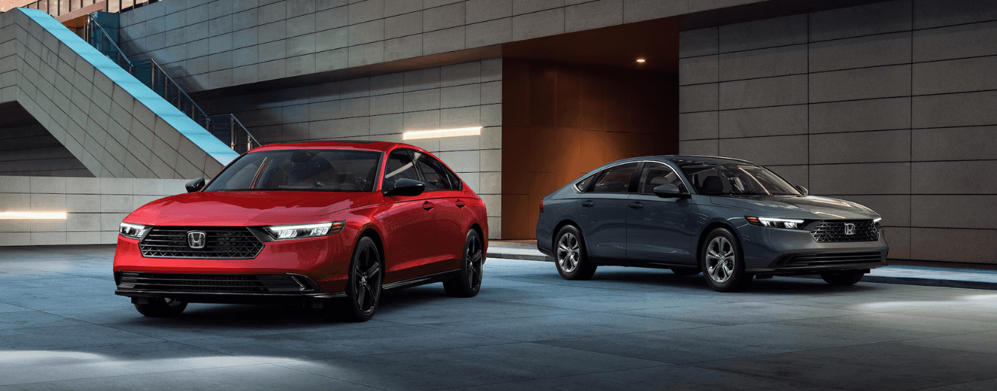 Two 2025 Honda Accord's, one red one grey, parked side by side at an angle underneath an overhand.