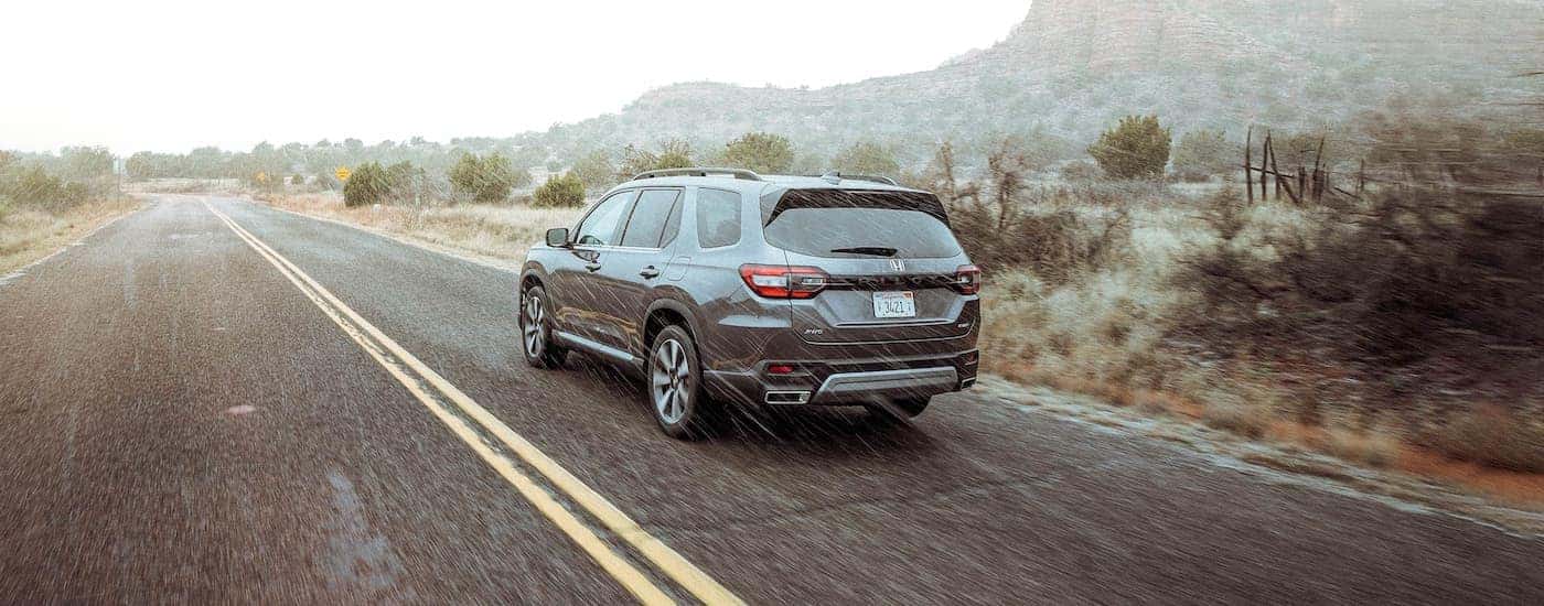Rear of a grey 2025 Honda Pilot Elite driving down a road.