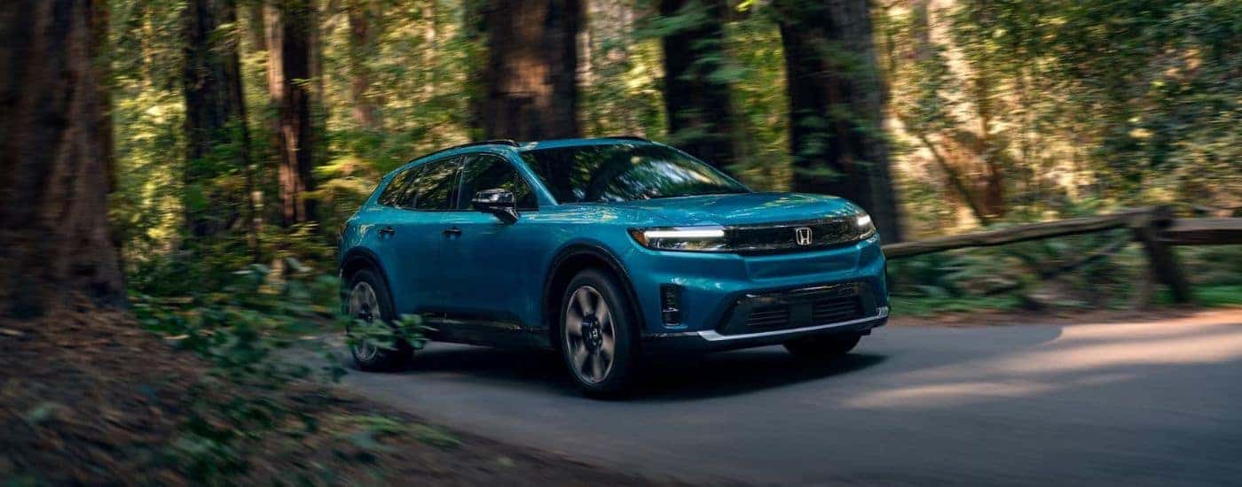 Blue 2025 Honda Prologue driving through a forest.