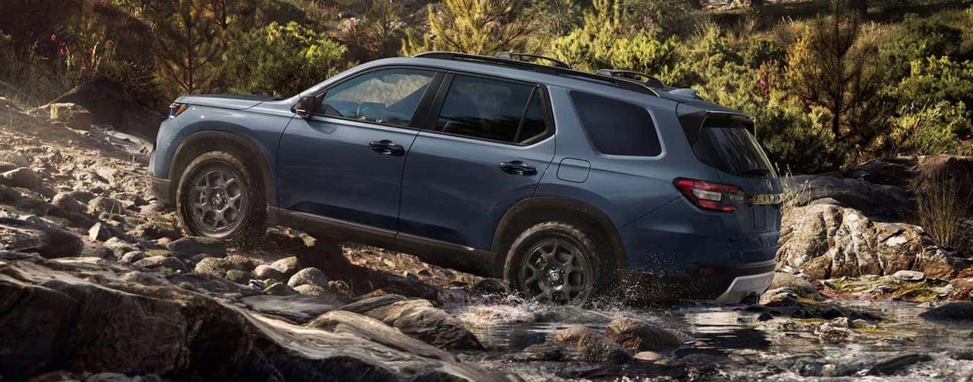 Side of a blue 2026 Honda Pilot off-roading on a rocky trail