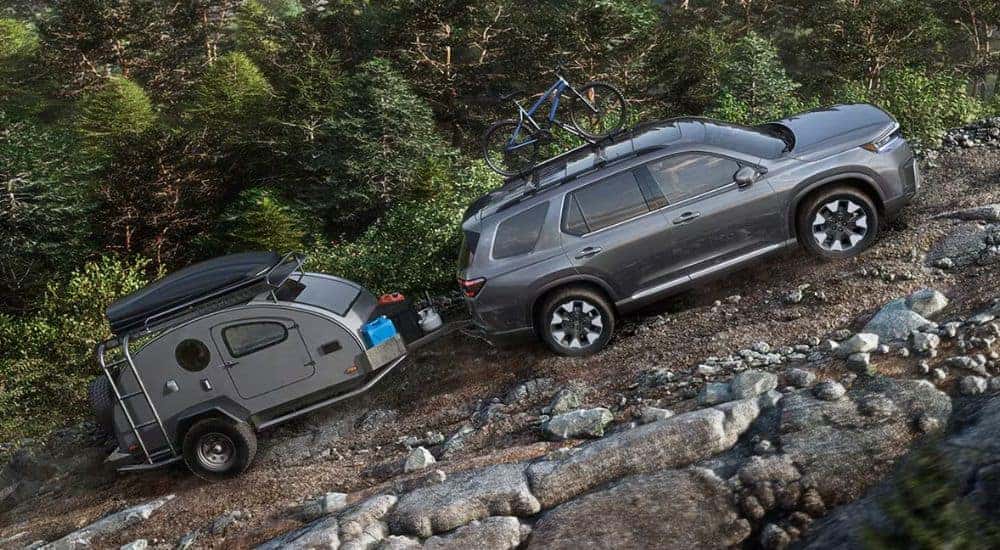Grey 2026 Honda Pilot towing a camper up a rocky hill