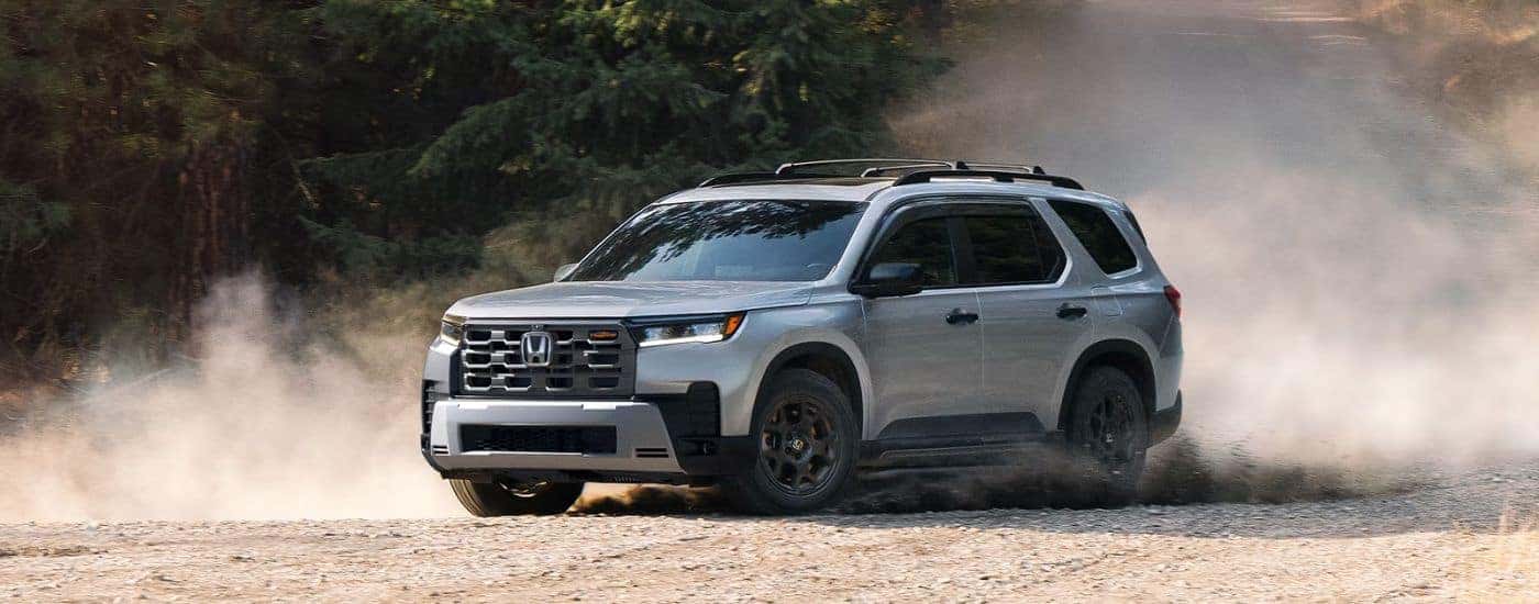 Silver 2026 Honda Pilot Trailsport driving on a dirt road.