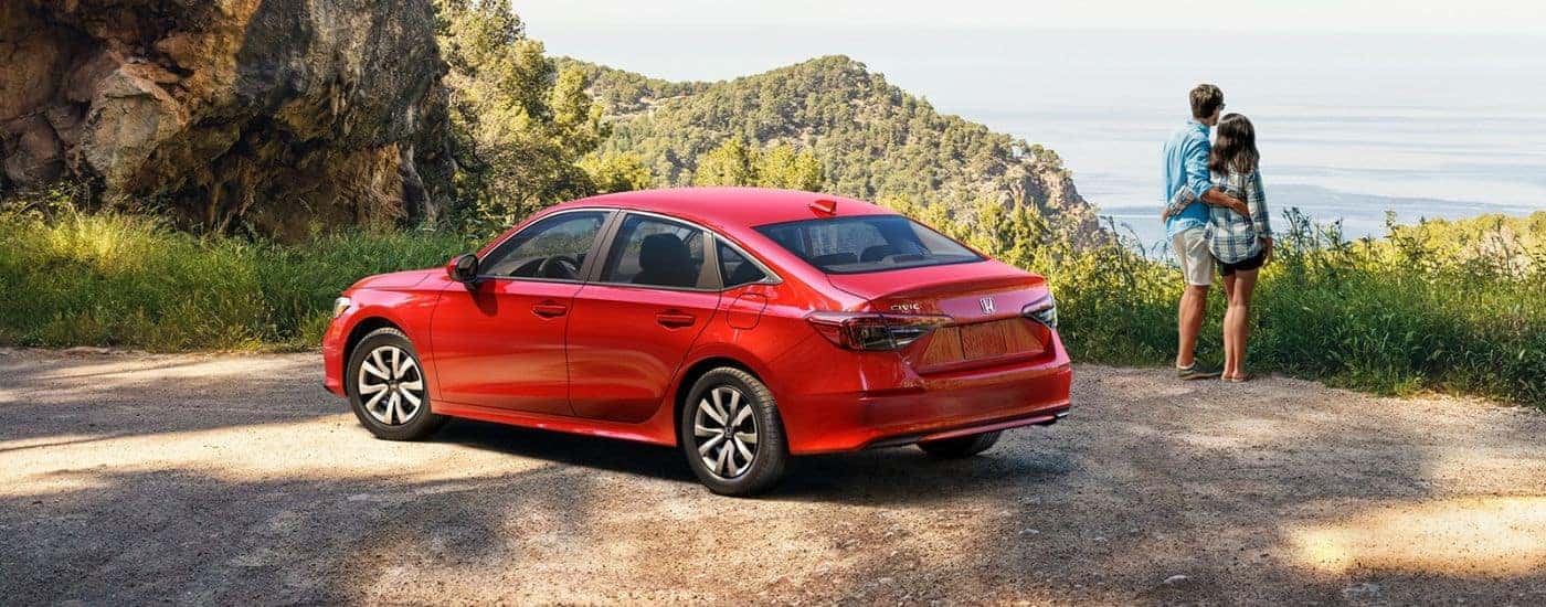 Red 2026 Honda Civic Sedan parked by a scenic view and two people.