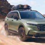 A green 2026 Honda CR-V TrailSport shown driving a dirt road.