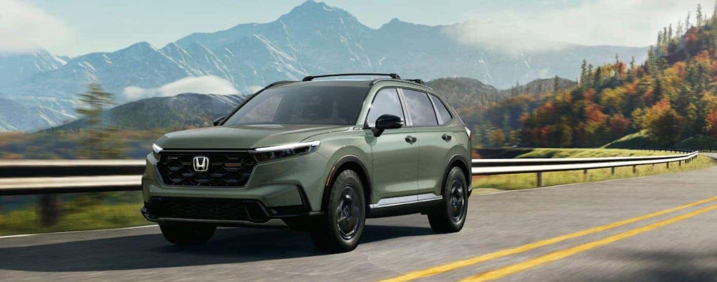 A green 2026 Honda CR-V Hybrid TrailSport shown driving by mountains.
