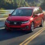A red 2027 Honda Odyssey Elite driving by a lake.