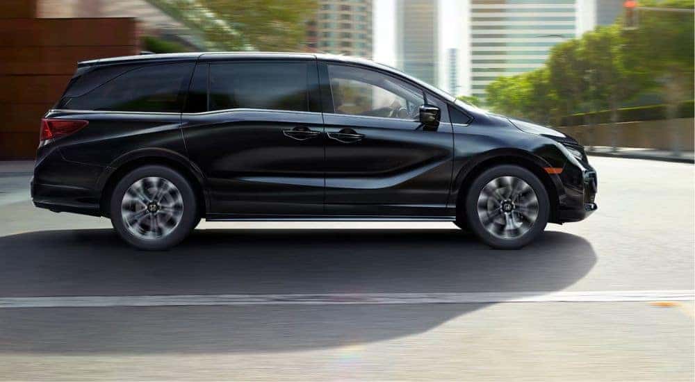 Side view of a black 2027 Honda Odyssey Elite driving.