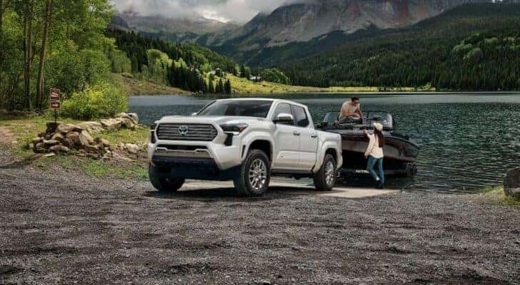 A white 2024 Toyota Tacoma Limited is shown towing a boat near water.