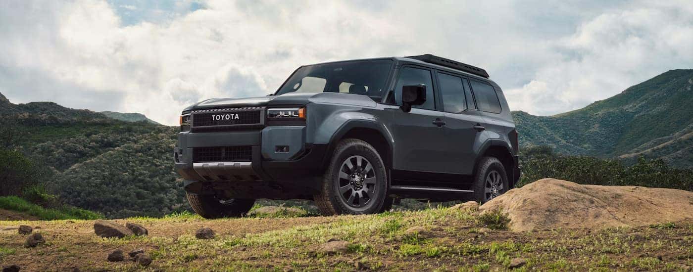 A slate blue 2024 Toyota Land Cruiser parked on a grassy knoll.