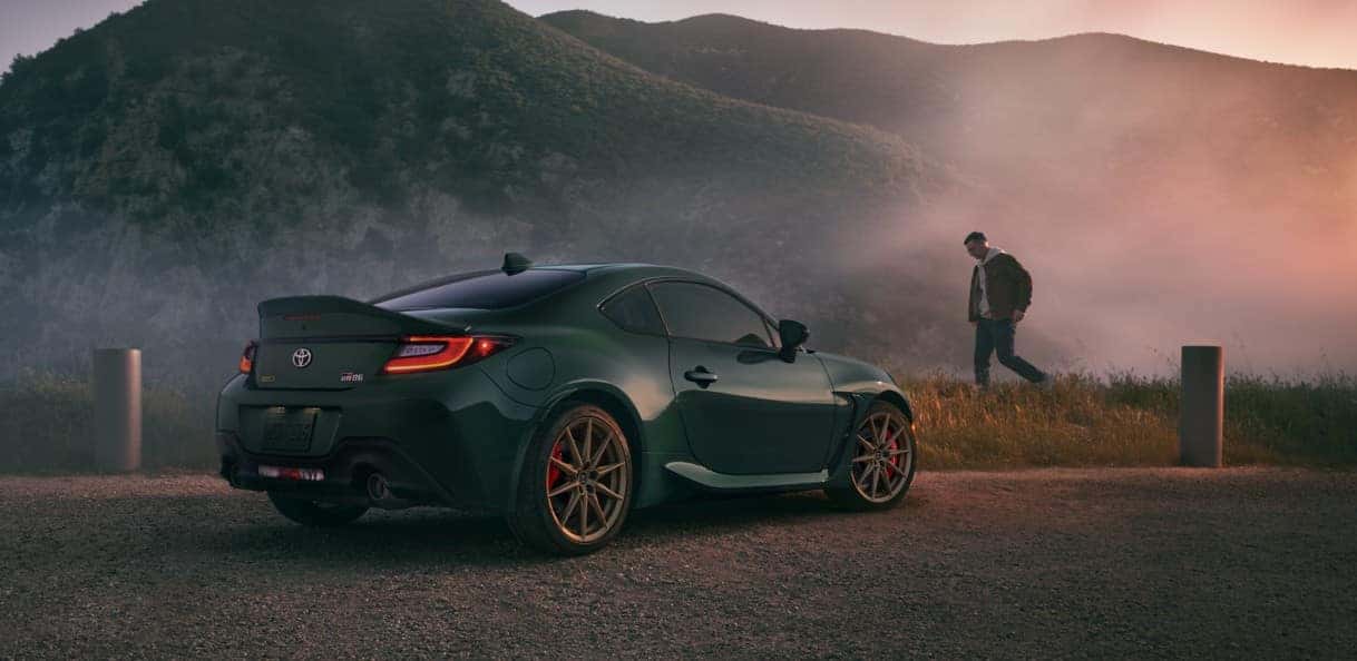 A green 2025 Toyota GR86 parked on the side of a road with a man walking by