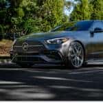 Matte gray 2026 Mercedes-Benz C-Class sedan driving on a tree-lined street.