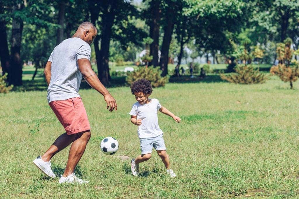 Father and son playing soccer together at a local park