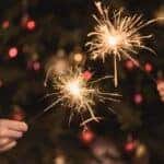 Two people holding sparklers in front of holiday decorations