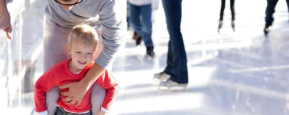 Child ice skating with guardian at a crowded rink on a sunny day