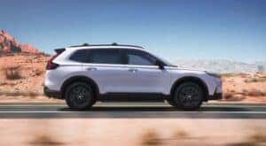 A white 2024 Honda CR-V Sport Touring Hybrid is shown driving on a sunny day.