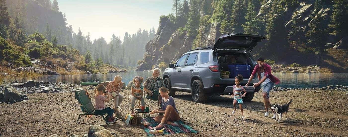 A popular Honda Pilot for sale in North Richland Hills, a gray 2023 Honda Pilot TrailSport, is shown parked near a family picnicking.